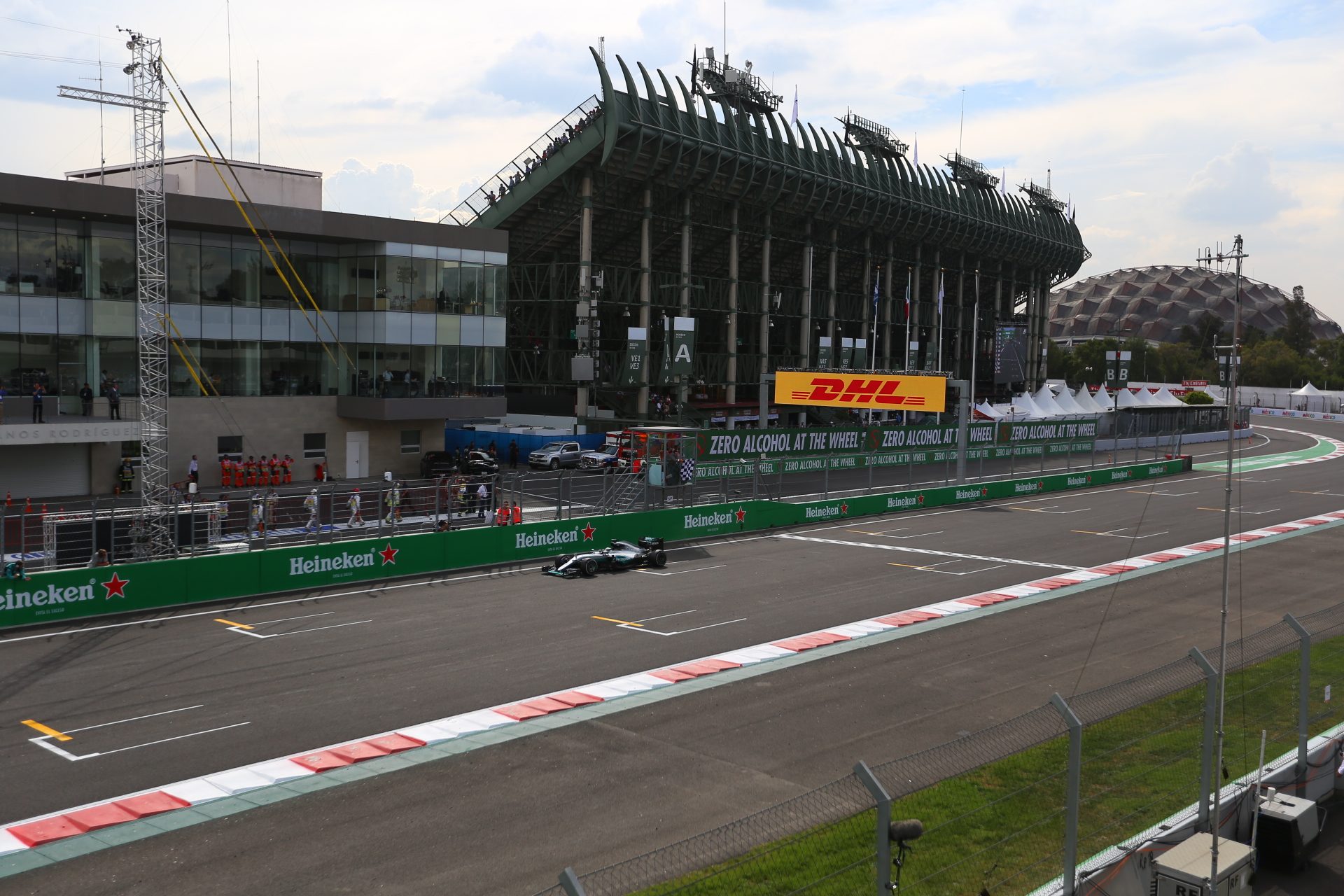 A car on the main straight at the Autódromo Hermanos Rodríguez during the 2016 Mexican Grand Prix, with the pit building and grandstand behind